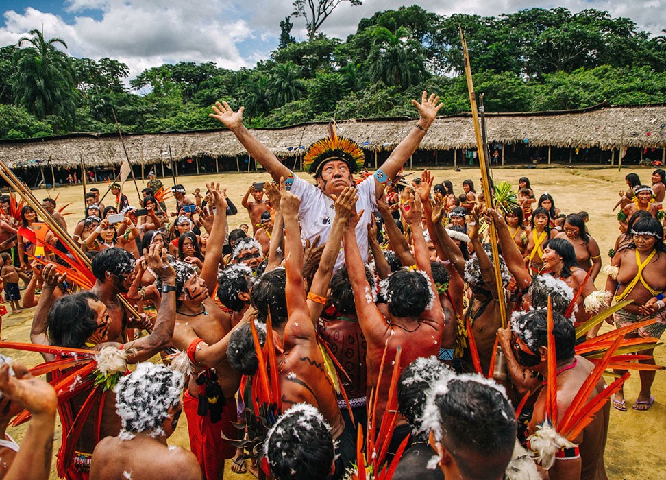 An Indigenous community celebration in the Amazon, a leader lifted with arms raised
