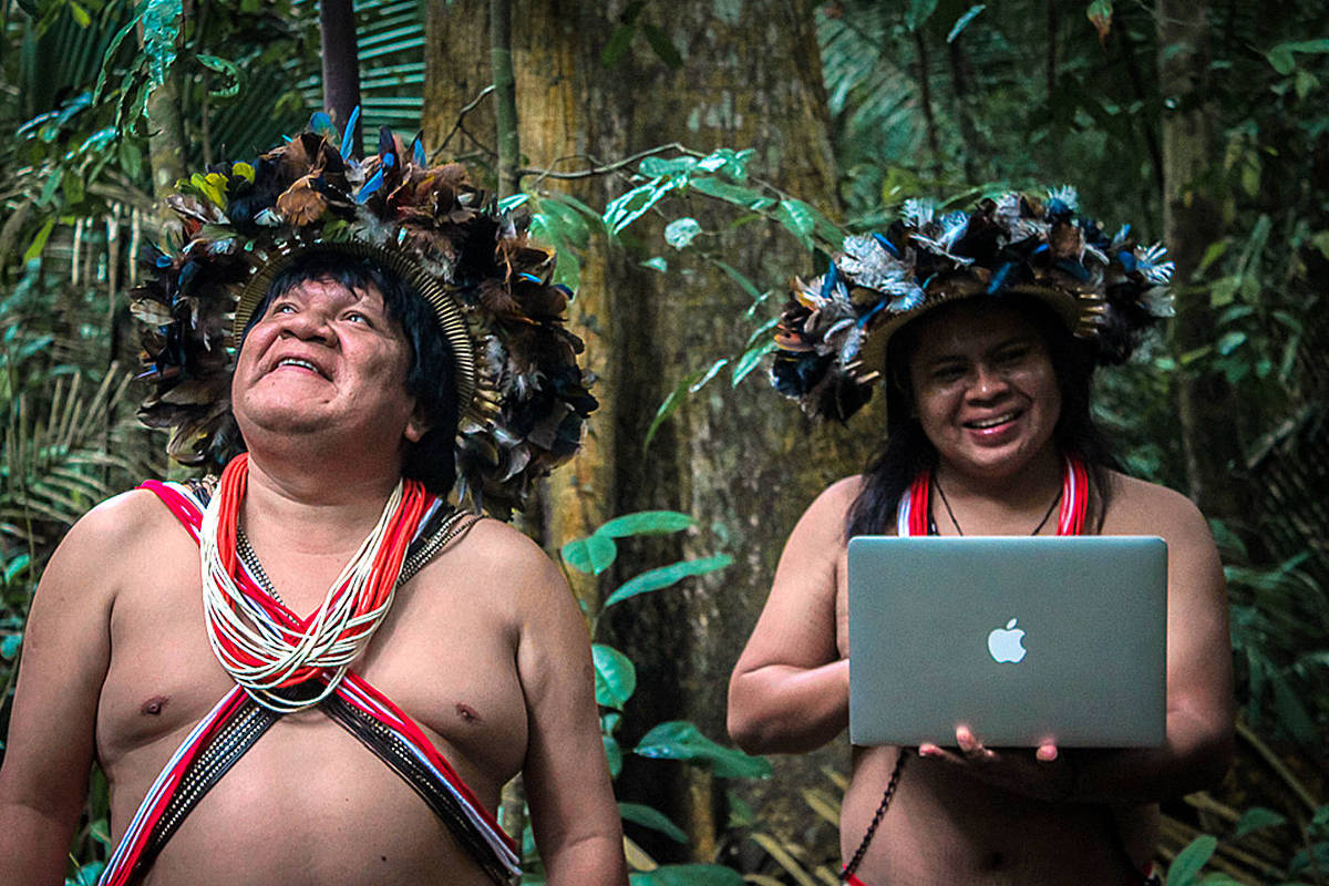 Two Indigenous community scientists in the Amazon rainforest, one holding a laptop
