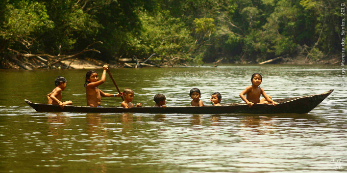 Indigenous children paddling a canoe along an Amazon river